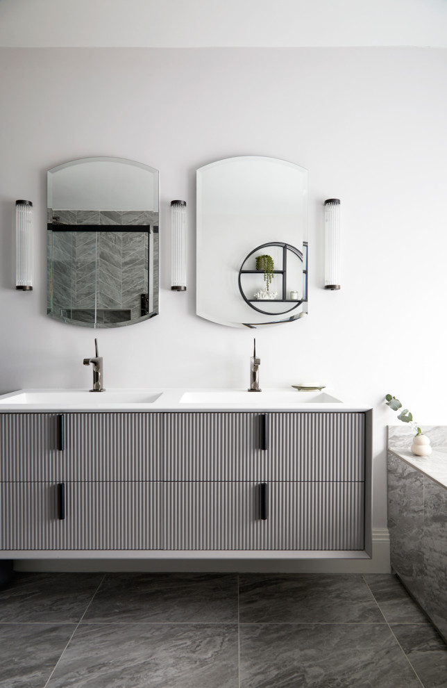 Modern inredning av ett stort vit vitt en-suite badrum, med luckor med profilerade fronter, grå skåp, ett platsbyggt badkar, en kantlös dusch, en vägghängd toalettstol, grå kakel, keramikplattor, grå väggar, klinkergolv i keramik, ett väggmonterat handfat, bänkskiva i akrylsten, grått golv och dusch med gångjärnsdörr