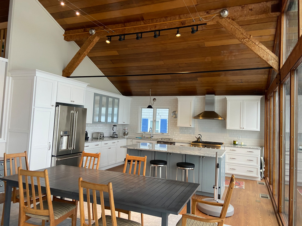 This is an example of a large beach style l-shaped open plan kitchen in Boston with an undermount sink, shaker cabinets, white cabinets, granite benchtops, white splashback, subway tile splashback, stainless steel appliances, light hardwood floors, with island, brown floor, grey benchtop, exposed beam, vaulted and wood.
