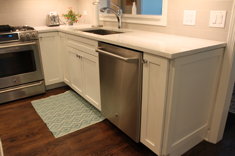 Example of a mid-sized transitional l-shaped dark wood floor and brown floor enclosed kitchen design in Chicago with an undermount sink, recessed-panel cabinets, white cabinets, quartzite countertops, white backsplash, subway tile backsplash, stainless steel appliances and an island