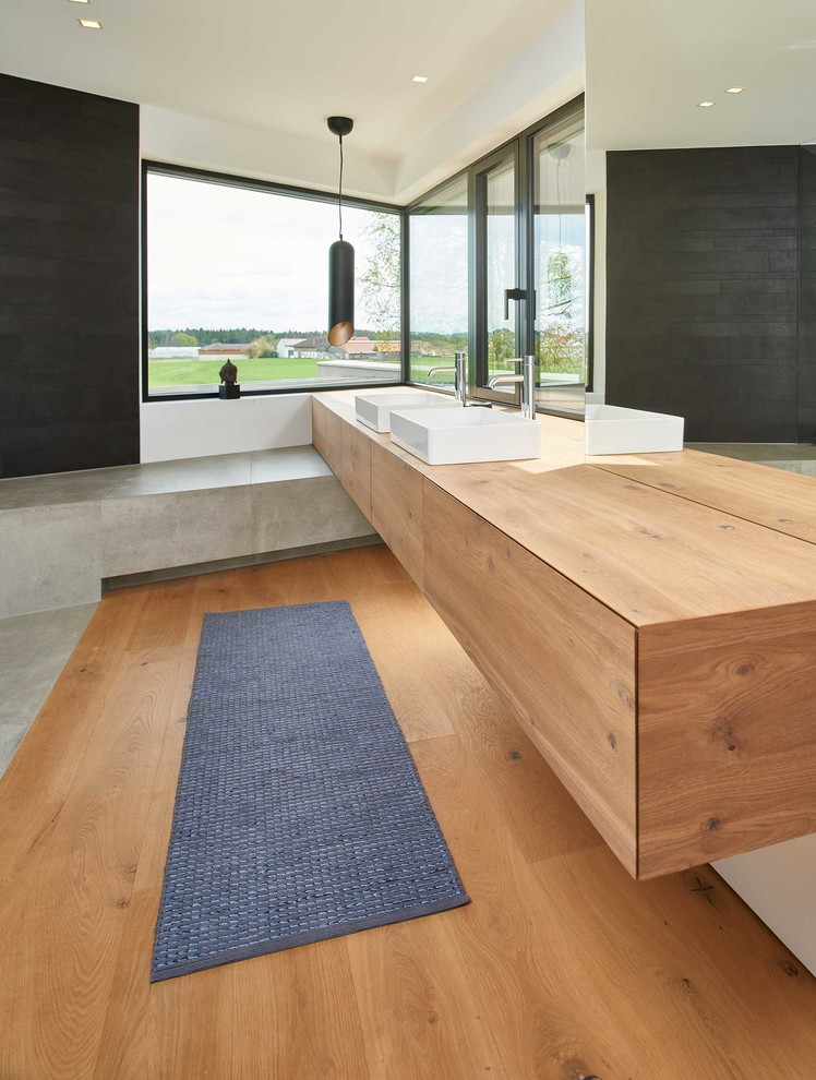 Design ideas for a mid-sized contemporary bathroom in Stuttgart with flat-panel cabinets, medium wood cabinets, black tile, white walls, medium hardwood floors, a vessel sink, wood benchtops, brown floor and brown benchtops.
