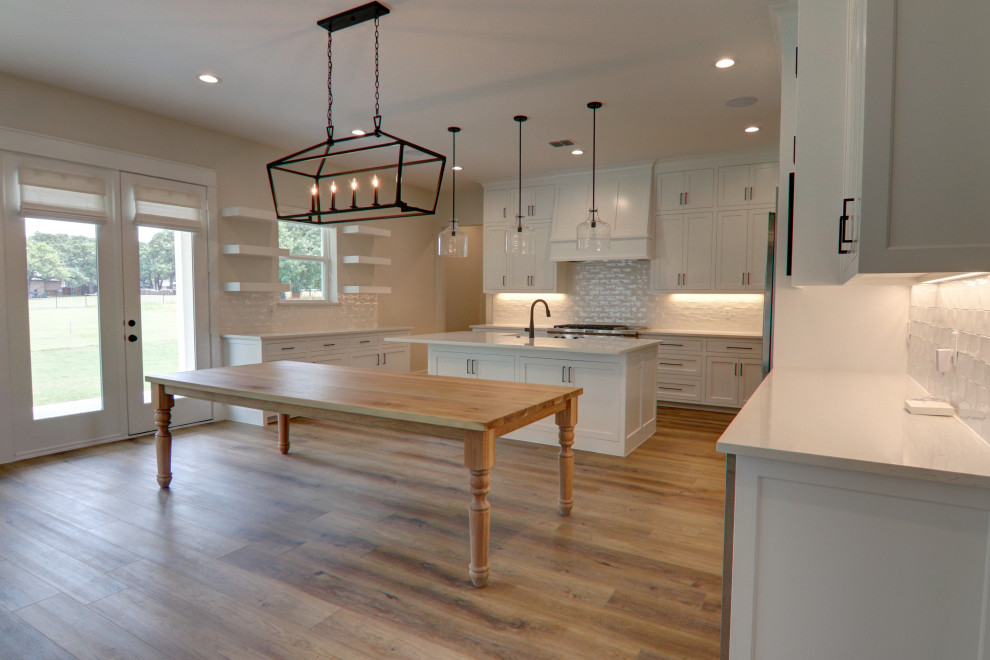 Design ideas for a large transitional u-shaped eat-in kitchen in Dallas with a farmhouse sink, flat-panel cabinets, white cabinets, quartz benchtops, white splashback, ceramic splashback, stainless steel appliances, vinyl floors, with island, brown floor and white benchtop.