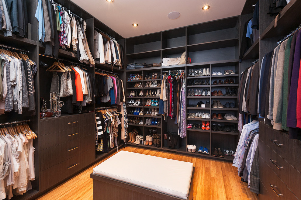 Photo of a large modern gender-neutral walk-in wardrobe in Calgary with flat-panel cabinets, dark wood cabinets and bamboo floors.