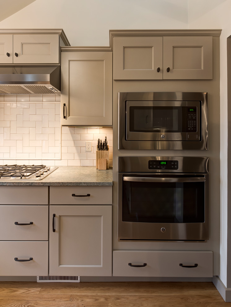 Mid-sized traditional l-shaped kitchen pantry in Boston with a farmhouse sink, recessed-panel cabinets, beige cabinets, granite benchtops, beige splashback, subway tile splashback, stainless steel appliances, medium hardwood floors, no island and brown floor.