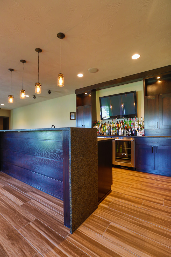 This is an example of a large arts and crafts galley seated home bar in Other with shaker cabinets, dark wood cabinets, quartzite benchtops and porcelain floors.