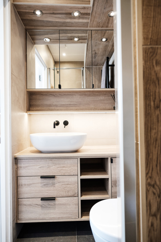 Inspiration for a small modern master bathroom in London with flat-panel cabinets, medium wood cabinets, a curbless shower, a wall-mount toilet, gray tile, porcelain tile, grey walls, porcelain floors, a vessel sink, laminate benchtops, black floor, a hinged shower door, a single vanity and a built-in vanity.
