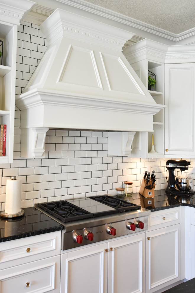 Inspiration for a traditional l-shaped open plan kitchen in Edmonton with an undermount sink, shaker cabinets, white cabinets, granite benchtops, white splashback, subway tile splashback, stainless steel appliances, ceramic floors, black floor, black benchtop and multiple islands.