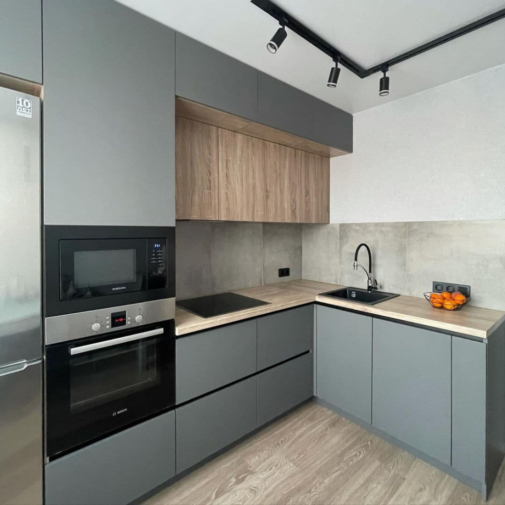 Medium sized contemporary l-shaped kitchen/diner in Moscow with a built-in sink, flat-panel cabinets, green cabinets, wood worktops, grey splashback, porcelain splashback, black appliances, laminate floors, no island, brown floors and yellow worktops.