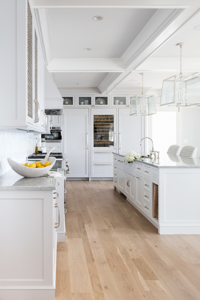 Inspiration for a large transitional l-shaped light wood floor and beige floor open concept kitchen remodel in Boston with a farmhouse sink, shaker cabinets, gray cabinets, quartz countertops, white backsplash, subway tile backsplash, paneled appliances, an island and gray countertops