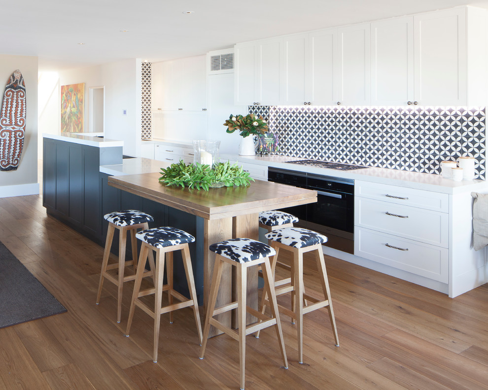 Photo of a large beach style galley eat-in kitchen in Sydney with a double-bowl sink, shaker cabinets, white cabinets, quartz benchtops, brown splashback, ceramic splashback, stainless steel appliances, medium hardwood floors and with island.