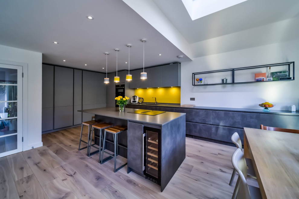 Exemple d'une grande cuisine ouverte moderne en L avec un placard à porte plane, des portes de placard grises, un plan de travail en quartz modifié, une crédence jaune, un électroménager noir, îlot et un plan de travail gris.
