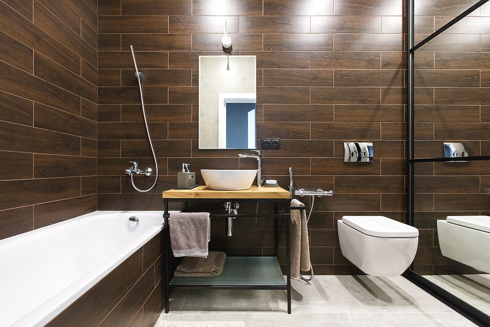 Esempio di una stanza da bagno industriale di medie dimensioni con WC sospeso, piastrelle marroni, piastrelle in gres porcellanato, pareti marroni, pavimento in gres porcellanato, lavabo da incasso, top in legno e pavimento grigio