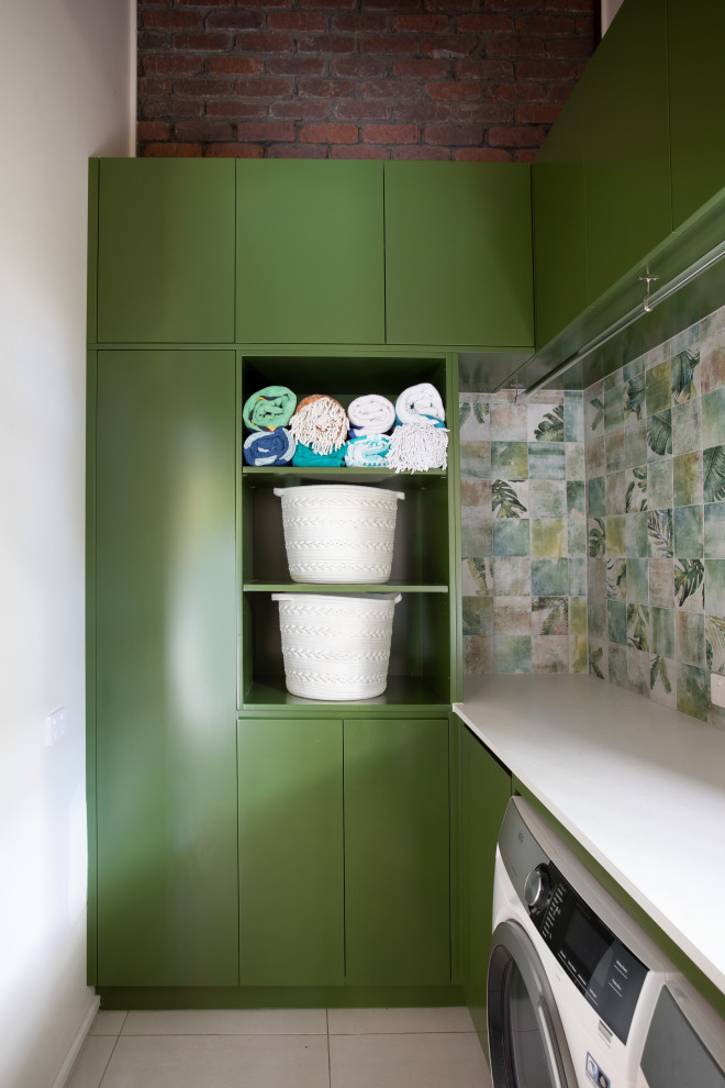 Idéer för att renovera en liten funkis vita l-formad vitt tvättstuga, med en nedsänkt diskho, gröna skåp, bänkskiva i kvarts, grönt stänkskydd, stänkskydd i porslinskakel, flerfärgade väggar, klinkergolv i porslin, en tvättmaskin och torktumlare bredvid varandra och grått golv