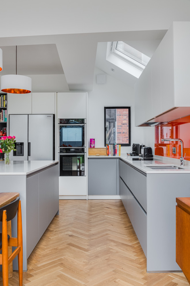 Photo of a large contemporary eat-in kitchen in London with a drop-in sink, grey cabinets, quartzite benchtops, orange splashback, glass sheet splashback, coloured appliances, light hardwood floors, brown floor, white benchtop and vaulted.