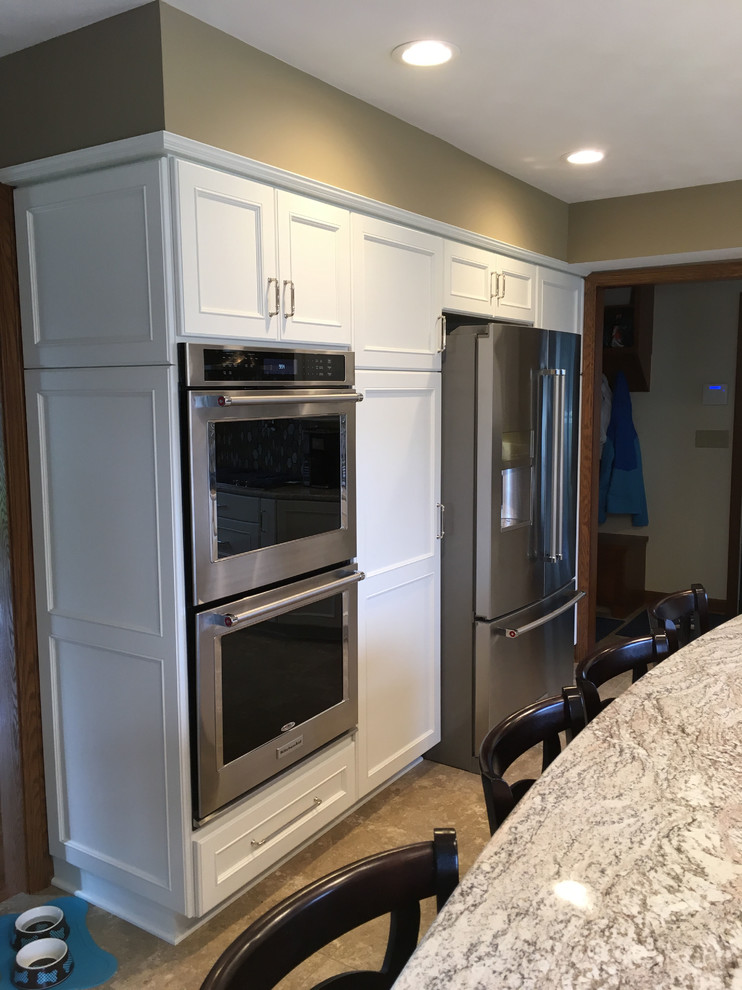 Example of a large transitional l-shaped vinyl floor and beige floor eat-in kitchen design with a double-bowl sink, recessed-panel cabinets, white cabinets, granite countertops, brown backsplash, ceramic backsplash, stainless steel appliances and an island