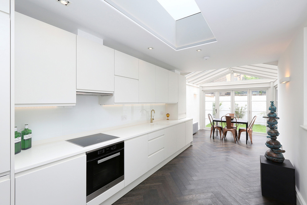 Inspiration for a large contemporary galley eat-in kitchen in London with flat-panel cabinets, white cabinets, white splashback, medium hardwood floors, no island, brown floor and white benchtop.