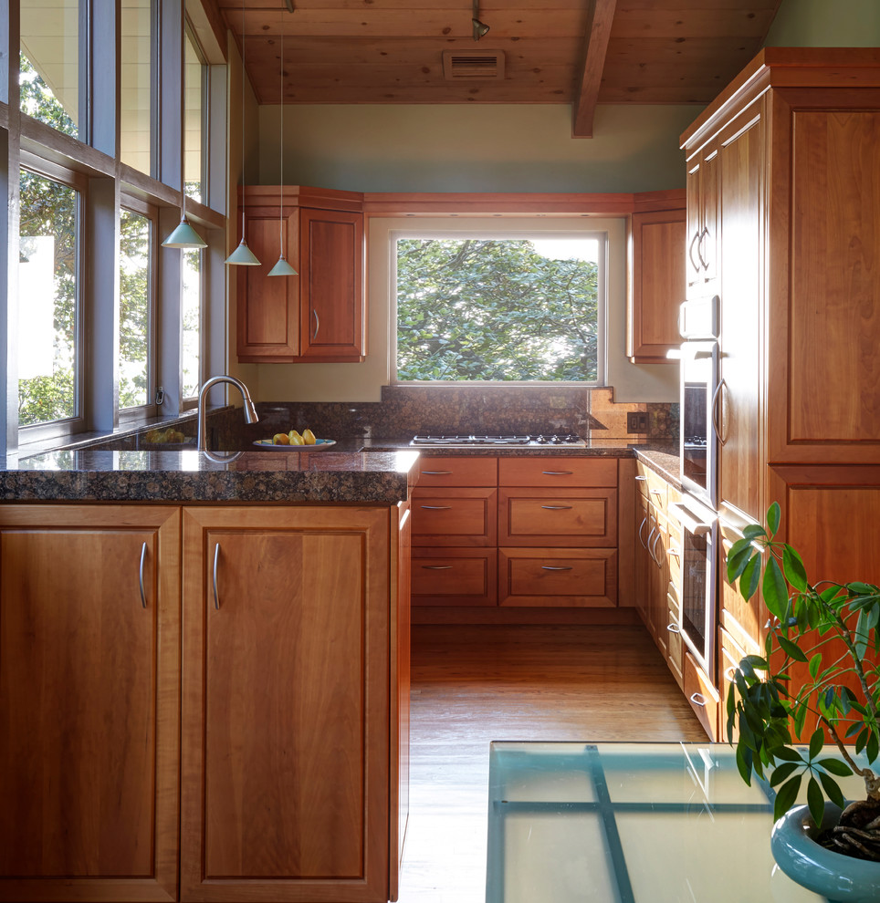 This is an example of a mid-sized midcentury u-shaped separate kitchen in San Francisco with an undermount sink, raised-panel cabinets, medium wood cabinets, granite benchtops, brown splashback, stone slab splashback, panelled appliances, light hardwood floors, no island, brown floor and brown benchtop.