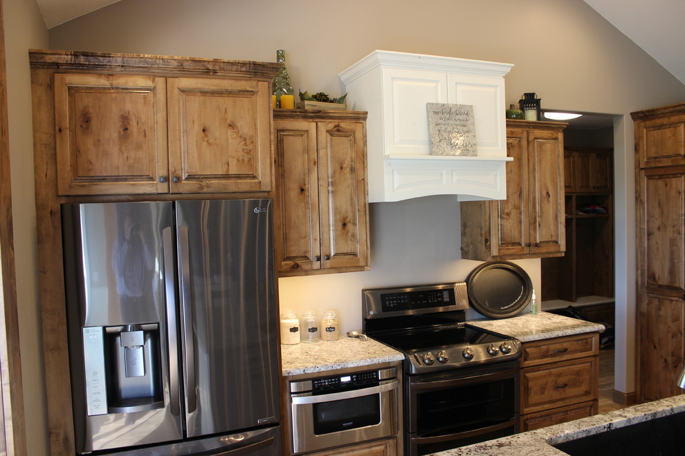 Open concept kitchen - large rustic l-shaped medium tone wood floor and brown floor open concept kitchen idea with an undermount sink, raised-panel cabinets, medium tone wood cabinets, granite countertops, stainless steel appliances and an island