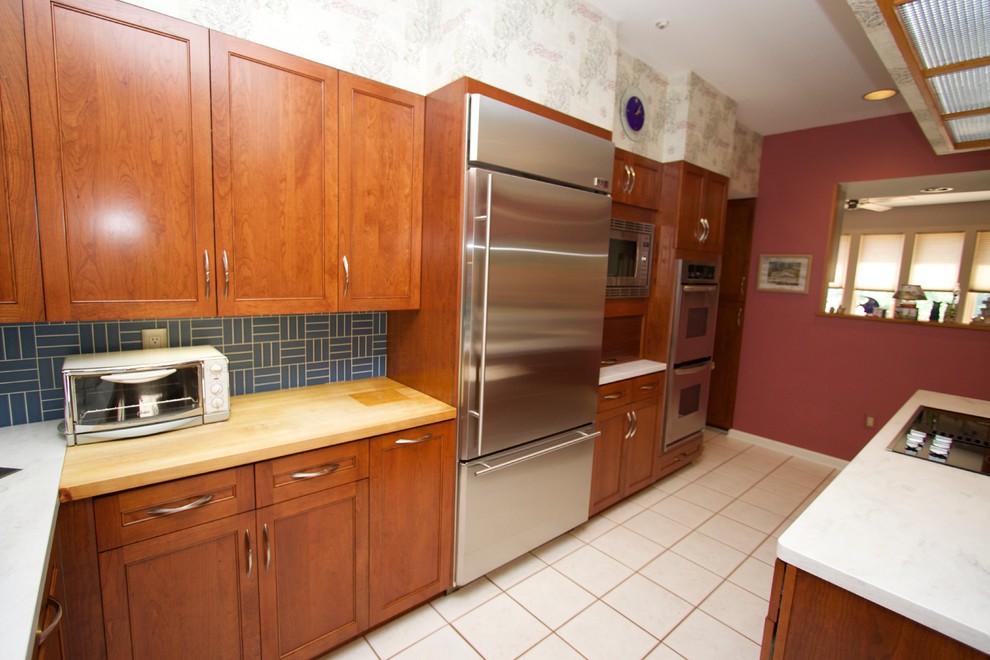 Transitional l-shaped ceramic tile open concept kitchen photo in Baltimore with an undermount sink, recessed-panel cabinets, medium tone wood cabinets, solid surface countertops, blue backsplash, ceramic backsplash, stainless steel appliances and an island