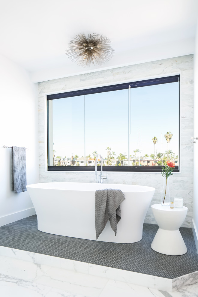 Inspiration for a large modern master bathroom in Los Angeles with flat-panel cabinets, medium wood cabinets, a freestanding tub, a double shower, a one-piece toilet, gray tile, marble, white walls, marble floors, a vessel sink, solid surface benchtops, grey floor and a hinged shower door.