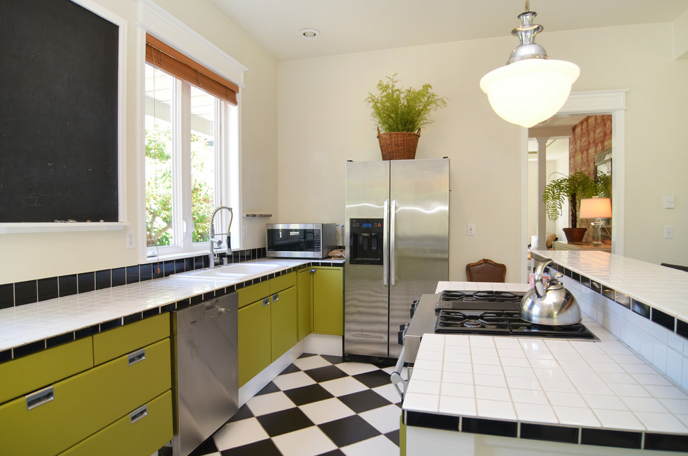 Photo of a large traditional kitchen in Seattle with a drop-in sink, green cabinets, tile benchtops, black splashback, ceramic splashback, stainless steel appliances, porcelain floors and with island.