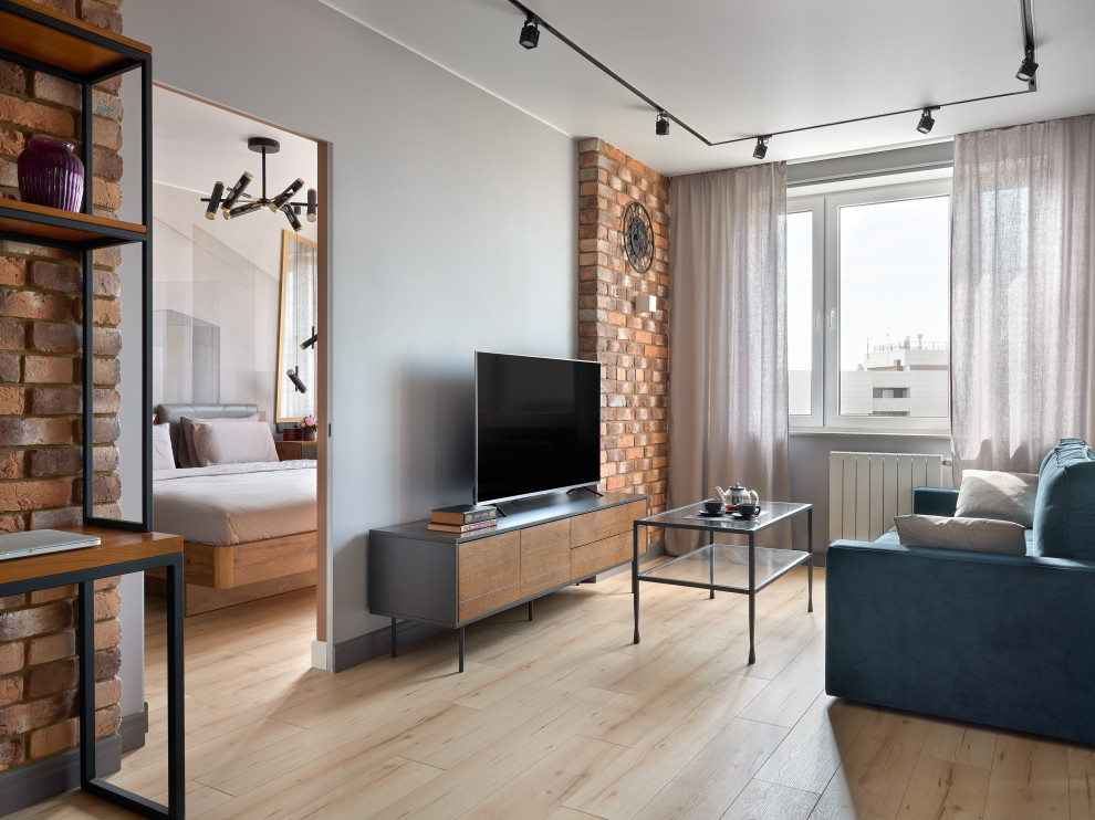 Пример оригинального дизайна: гостиная комната среднего размера в стиле лофт с коричневыми стенами, полом из ламината, зоной отдыха, коричневым полом, кирпичными стенами, синим диваном и отдельно стоящим телевизором