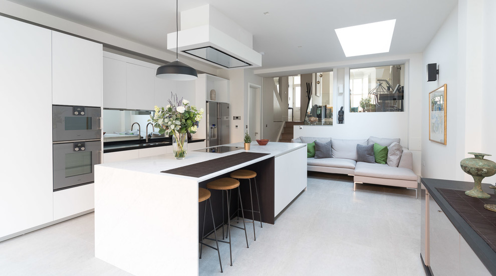 Inspiration for a mid-sized contemporary open plan kitchen in London with an undermount sink, flat-panel cabinets, white cabinets, mirror splashback, stainless steel appliances, with island and white floor.