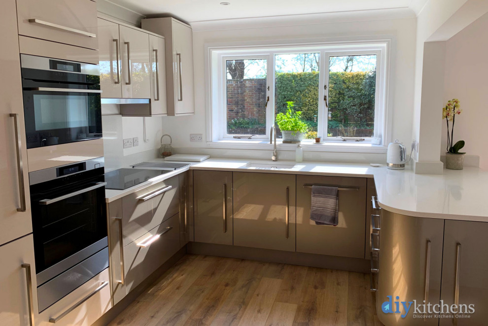 This is an example of a mid-sized modern u-shaped eat-in kitchen in West Midlands with flat-panel cabinets, beige cabinets, quartzite benchtops, no island and white benchtop.