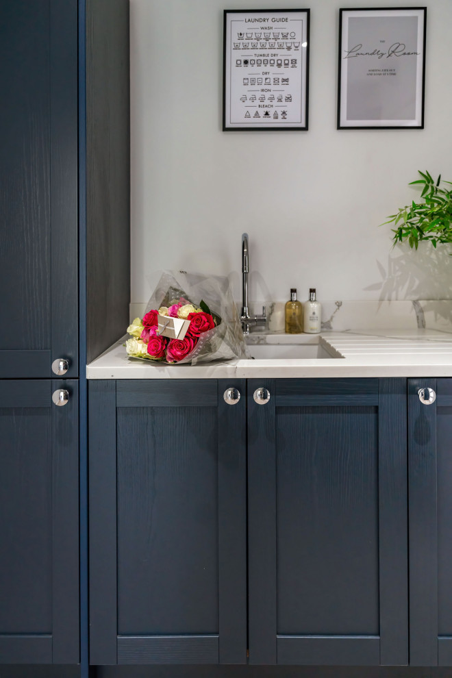 Modern inredning av en mellanstor liten tvättstuga, med en undermonterad diskho, skåp i shakerstil, blå skåp, bänkskiva i kvartsit, grå väggar, vinylgolv, en tvättmaskin och torktumlare bredvid varandra och grått golv