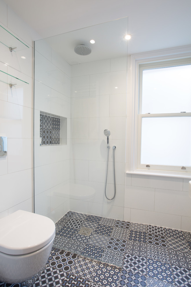 This is an example of a mid-sized scandinavian 3/4 wet room bathroom in London with flat-panel cabinets, white cabinets, a wall-mount toilet, white tile, porcelain tile, white walls, porcelain floors, a drop-in sink, multi-coloured floor, an open shower and a single vanity.