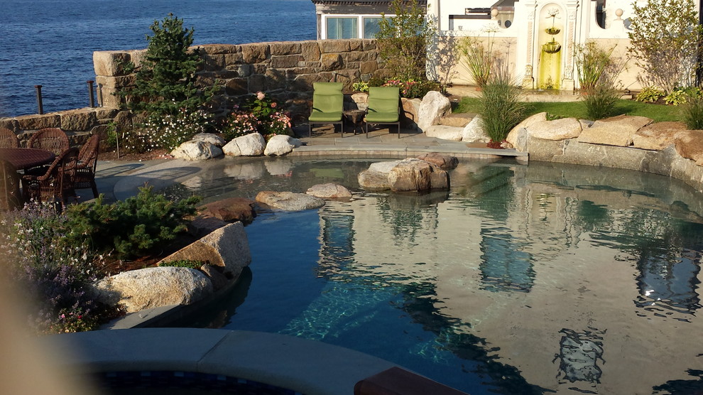 Expansive beach style side yard custom-shaped natural pool in Boston with a water feature and natural stone pavers.