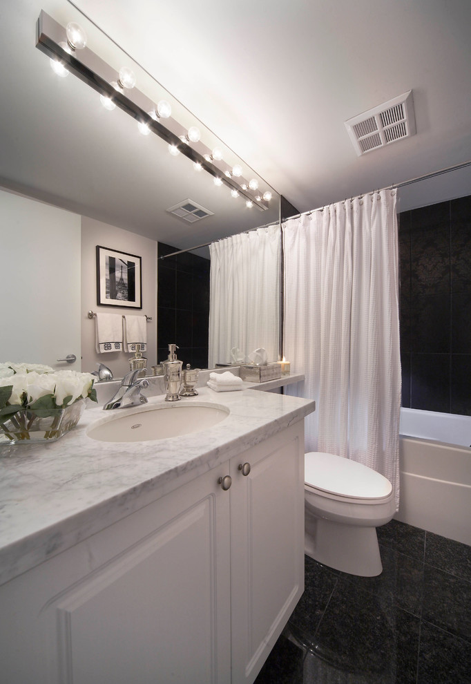 Photo of a transitional bathroom in Toronto with an undermount sink, raised-panel cabinets, white cabinets, marble benchtops, an alcove tub, a two-piece toilet, black tile and a shower curtain.