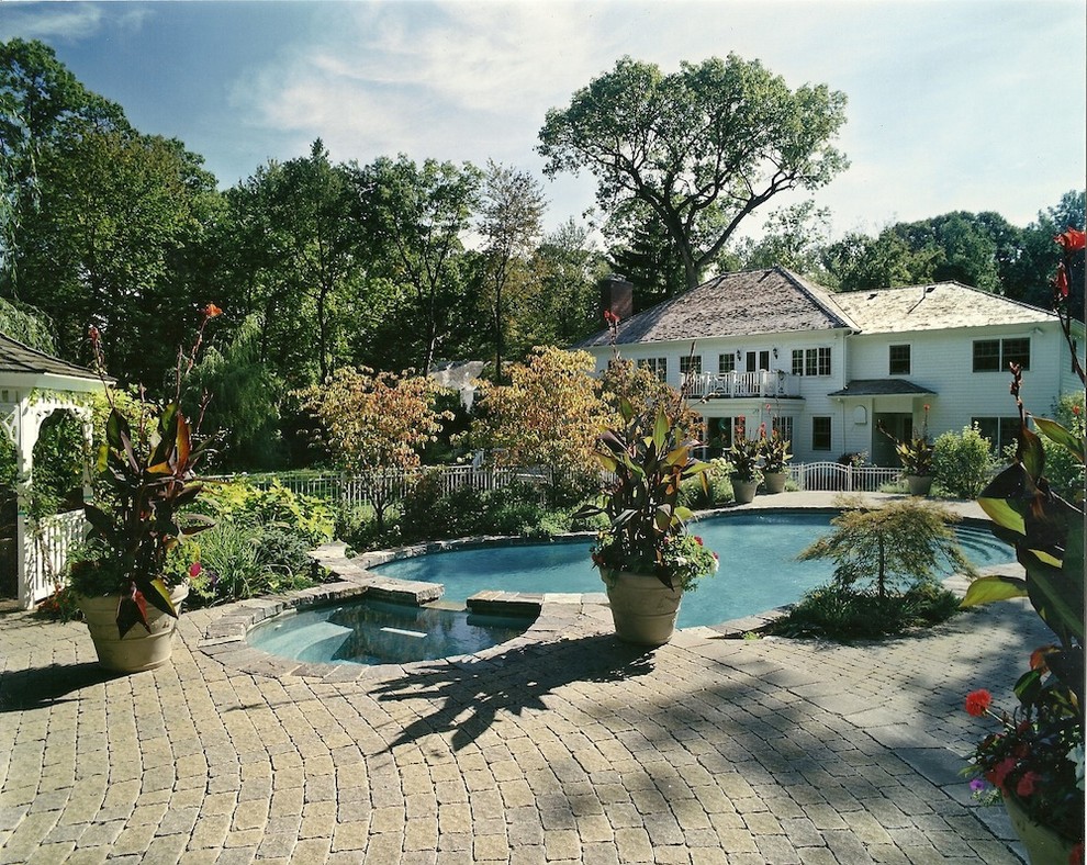 Inspiration for a large traditional backyard custom-shaped lap pool in New York with brick pavers and a hot tub.