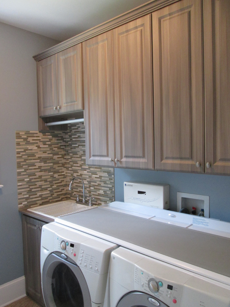 Photo of a mid-sized traditional single-wall utility room in Richmond with raised-panel cabinets, medium wood cabinets, solid surface benchtops, grey walls, light hardwood floors, a side-by-side washer and dryer and white benchtop.