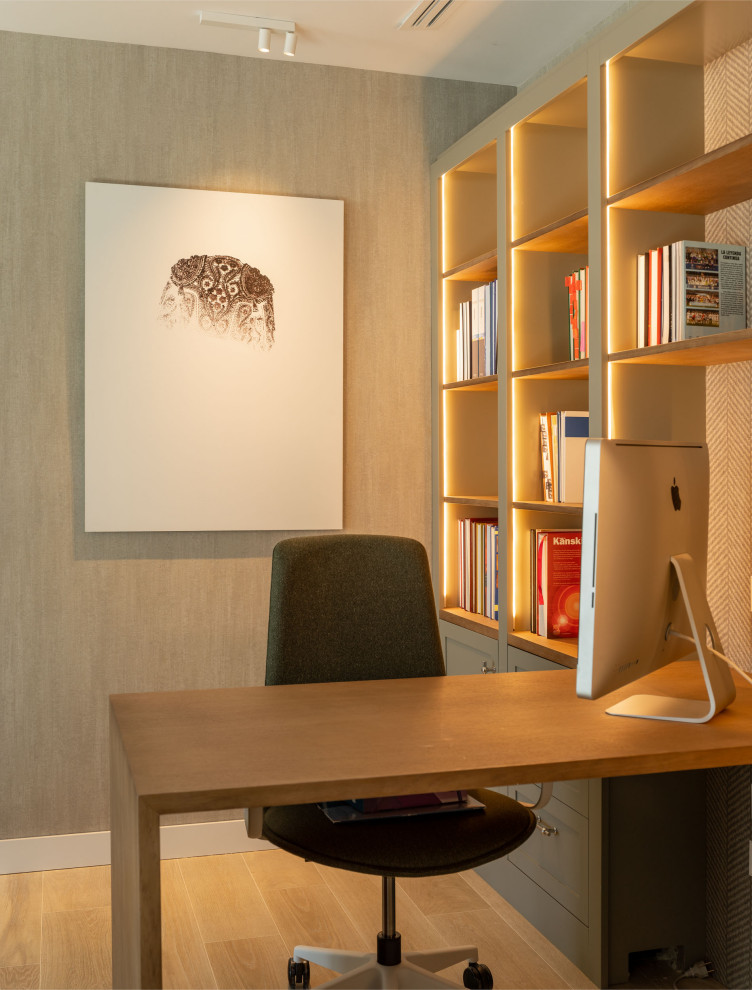Modelo de despacho actual de tamaño medio con paredes beige, suelo laminado, escritorio empotrado, suelo marrón y papel pintado