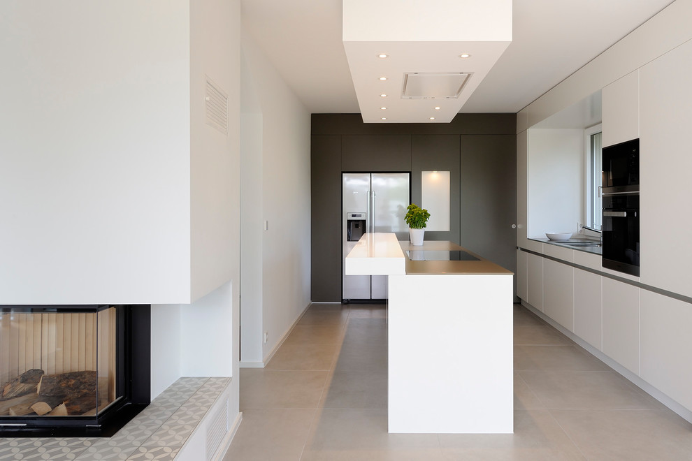 This is an example of a mid-sized contemporary galley open plan kitchen in Stuttgart with a drop-in sink, flat-panel cabinets, white cabinets, black appliances, cement tiles, multiple islands and beige floor.