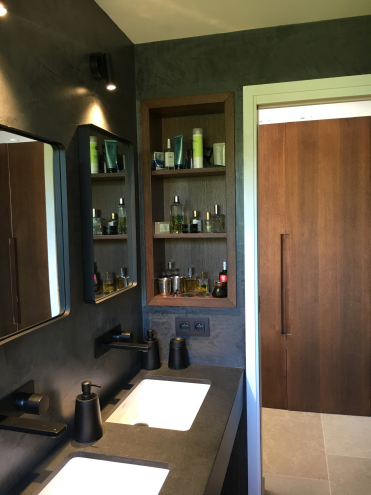 Cette image montre une petite salle d'eau design en bois brun avec un placard à porte affleurante, un mur noir, un sol en calcaire, un plan vasque, un plan de toilette en granite, un sol beige, un plan de toilette noir et meuble double vasque.