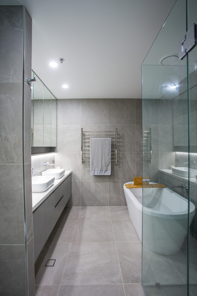 Design ideas for a mid-sized modern master bathroom in Brisbane with flat-panel cabinets, grey cabinets, a freestanding tub, a corner shower, a two-piece toilet, gray tile, porcelain tile, grey walls, porcelain floors, a vessel sink, engineered quartz benchtops, grey floor, a hinged shower door and white benchtops.