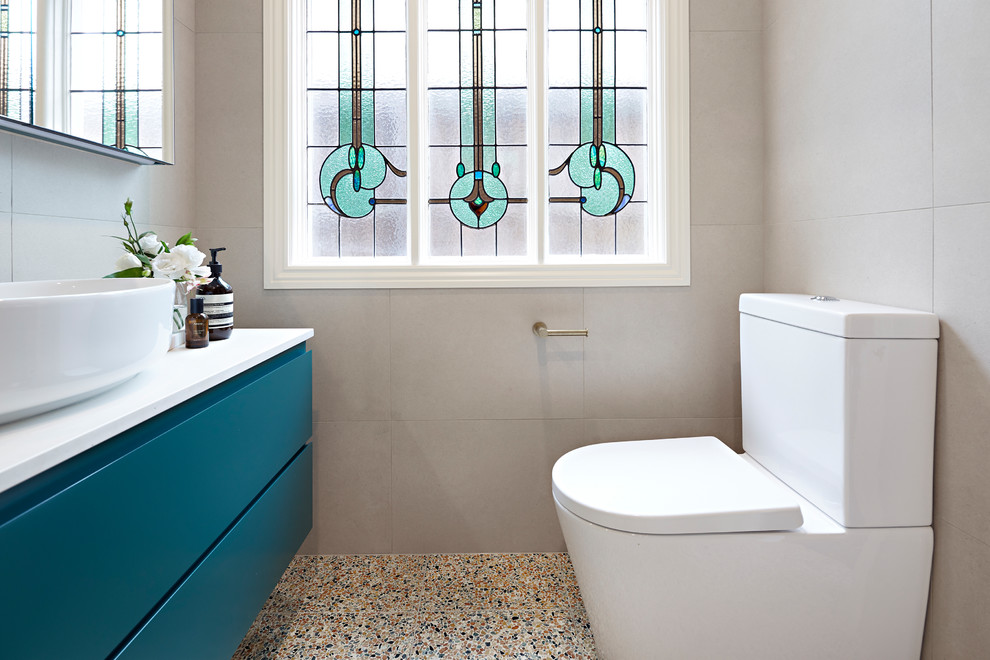 Small contemporary master bathroom in Melbourne with green cabinets, a shower/bathtub combo, a wall-mount toilet, beige tile, terrazzo floors, a hinged shower door, white benchtops, furniture-like cabinets, a drop-in tub, stone tile, beige walls, a vessel sink, engineered quartz benchtops and multi-coloured floor.