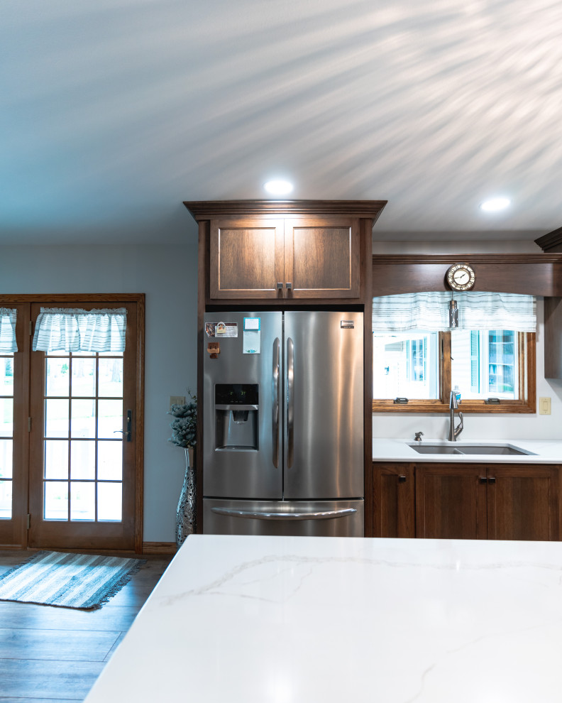 Example of a huge transitional l-shaped medium tone wood floor and brown floor open concept kitchen design with shaker cabinets, medium tone wood cabinets, quartz countertops, stainless steel appliances, an island and white countertops
