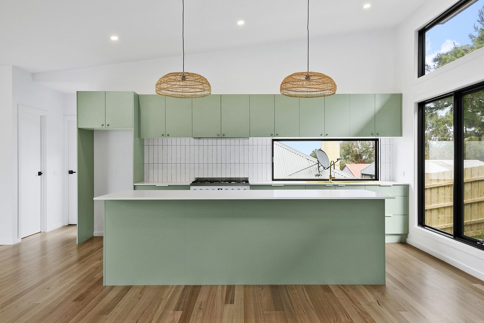 Photo of a mid-sized contemporary galley open plan kitchen in Melbourne with a double-bowl sink, flat-panel cabinets, green cabinets, quartz benchtops, white splashback, subway tile splashback, white appliances, medium hardwood floors, with island and white benchtop.