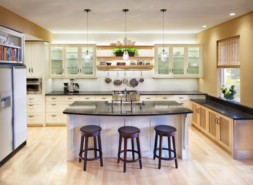 Photo of a large transitional u-shaped open plan kitchen in Minneapolis with a farmhouse sink, shaker cabinets, white cabinets, granite benchtops, white splashback, stainless steel appliances, light hardwood floors, with island and subway tile splashback.