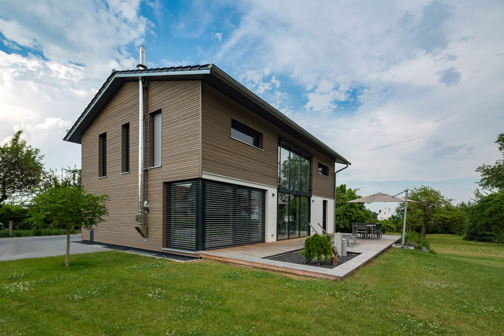 This is an example of a large contemporary two-storey grey house exterior in Munich with wood siding, a gable roof and a tile roof.