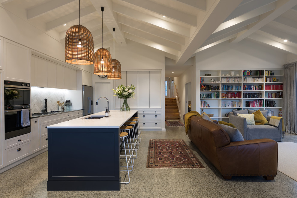 Mid-sized transitional l-shaped open plan kitchen in Auckland with concrete floors, grey floor, a double-bowl sink, recessed-panel cabinets, white cabinets, white splashback, stainless steel appliances, with island and white benchtop.
