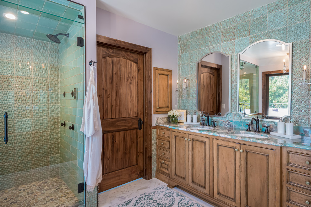 This is an example of a large transitional master bathroom in Milwaukee with furniture-like cabinets, medium wood cabinets, an alcove shower, a one-piece toilet, green tile, cement tile, purple walls, marble floors, an undermount sink, marble benchtops, white floor, a hinged shower door, blue benchtops, a double vanity, a built-in vanity and brick walls.