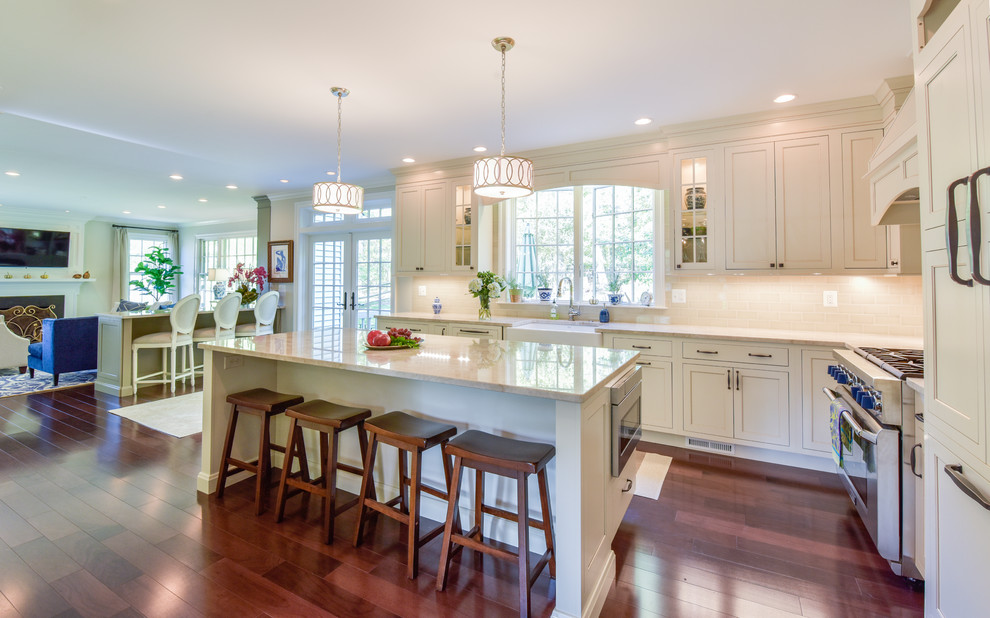 Photo of a large transitional l-shaped open plan kitchen in DC Metro with an undermount sink, beaded inset cabinets, white cabinets, quartz benchtops, beige splashback, subway tile splashback, panelled appliances, dark hardwood floors, with island and brown floor.