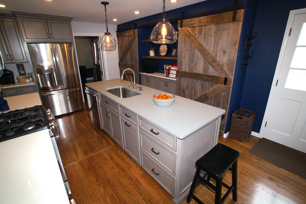 Photo of a mid-sized country galley eat-in kitchen in St Louis with a double-bowl sink, recessed-panel cabinets, grey cabinets, quartz benchtops, stainless steel appliances, medium hardwood floors and with island.