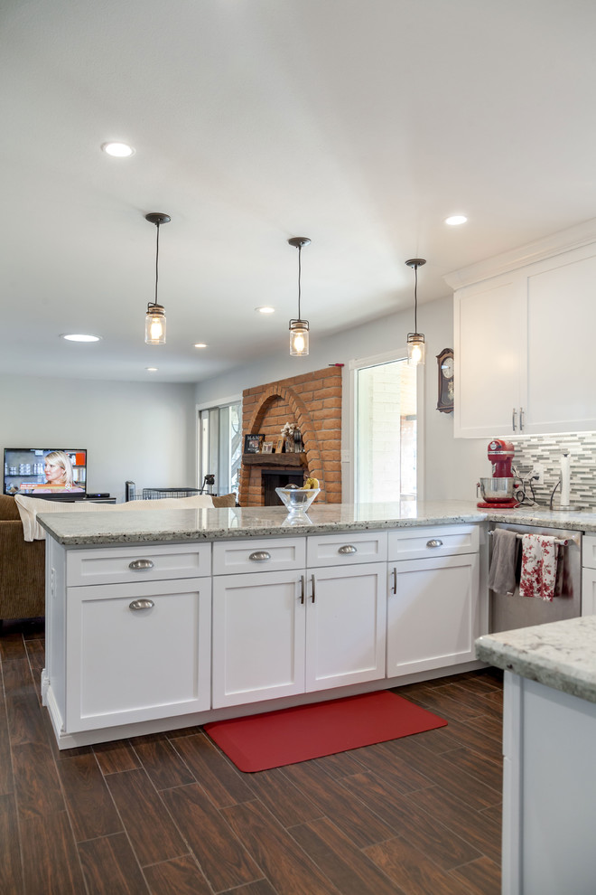 Inspiration for a mid-sized transitional u-shaped laminate floor and brown floor open concept kitchen remodel in Phoenix with an undermount sink, recessed-panel cabinets, white cabinets, granite countertops, multicolored backsplash, mosaic tile backsplash and stainless steel appliances