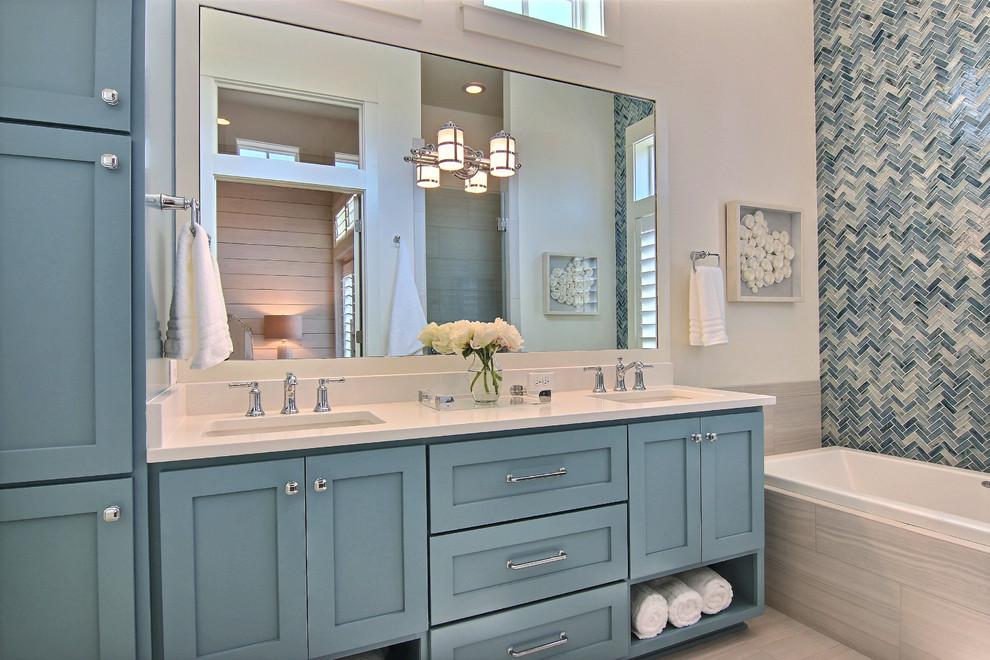 Inspiration for a mid-sized beach style bathroom in Austin with shaker cabinets, blue cabinets, a drop-in tub, an alcove shower, a one-piece toilet, blue tile, porcelain tile, white walls, porcelain floors, an undermount sink, quartzite benchtops, white floor and a hinged shower door.