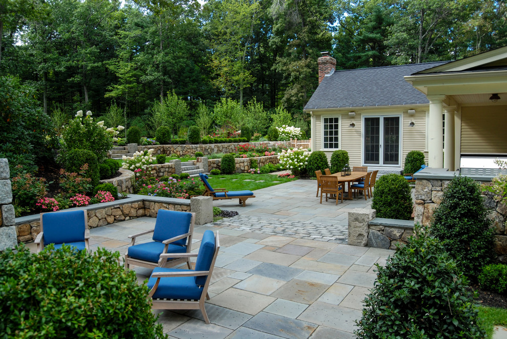 Photo of a mid-sized traditional backyard full sun garden in Boston with a retaining wall and natural stone pavers.