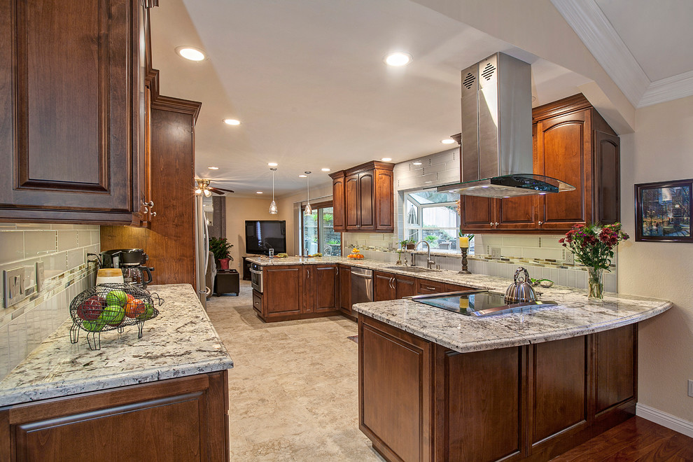 Inspiration for a mid-sized transitional u-shaped eat-in kitchen in San Diego with an undermount sink, raised-panel cabinets, brown cabinets, granite benchtops, grey splashback, ceramic splashback, stainless steel appliances, porcelain floors, a peninsula and beige floor.